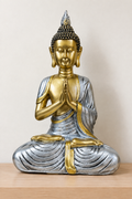 Buda plateado y dorado en oración sobre repisa de madera